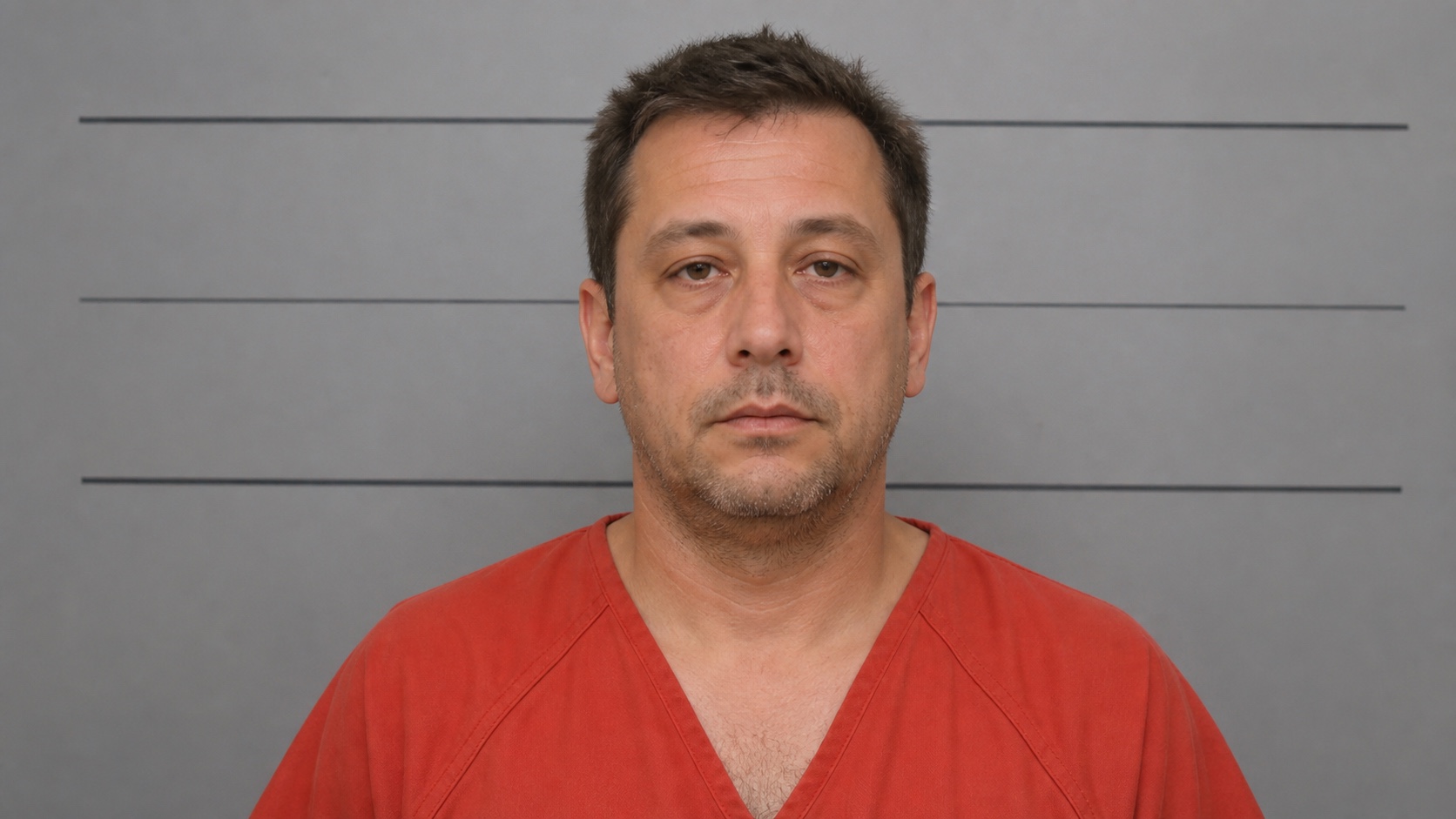A booking-style portrait of Daniel Reeve wearing an orange-red jail uniform.